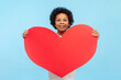© khosrork - Portrait of charming cute smiling little boy with curly hair holding big red hear demonstrating feelings to his classmate. Indoor studio shot isolated on blue background.