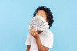 © khosrork - Portrait of rich little boy with curly hair holding smelling dollar banknotes huge amount of pocket money. Indoor studio shot isolated on blue background.