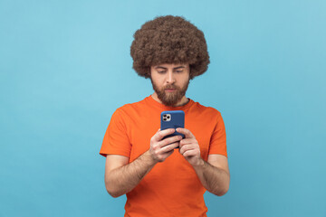 Wall Mural - portrait of concentrated man with afro hairstyle wearing orange t-shirt writing post on social netwo