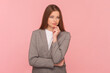 Portrait of pensive thoughtful beautiful woman with brown hair holding her chin, thinking, planning, looking away, wearing business suit. Indoor studio shot isolated on pink background.