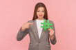 Portrait of smiling positive woman with brown hair holding pointing green hashtag, recommend community, wearing business suit. Indoor studio shot isolated on pink background.