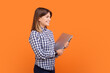 Profile portrait of confident happy optimistic woman with brown hair holding closed laptop, finishing online remote work, wearing checkered shirt. Indoor studio shot isolated on orange background