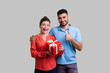 Portrait of couple standing together woman holding present box man showing like gesture, likes good gift, looking at camera. Indoor studio shot isolated on gray background.