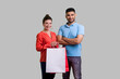 Portrait of pleased happy couple man and woman standing holding paper bags going shopping together in fashion mall. Indoor studio shot isolated on gray background.