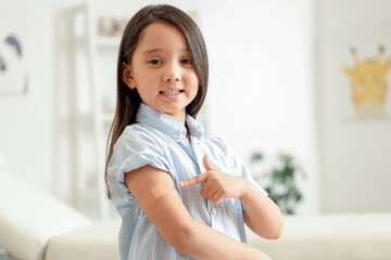 Canvas Print - Little Asian girl pointing at applied patch after vaccination in clinic