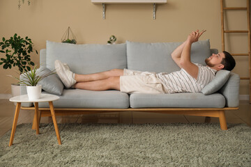 Canvas Print - Young man with mobile phone lying on sofa in living room