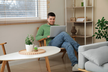 Wall Mural - Young man sitting on chair and using laptop in living room