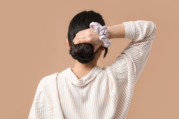 Wall Mural - Woman with bun hairstyle and silk scrunchy on beige background, back view