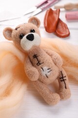 Wall Mural - Felted bear, wool and tools on white wooden table, closeup