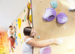 Shot of Europian girl while clambing artificial wall, top view. Europian female client of fitness room trains doing exercises on bouldering wall for climbing, active recreation