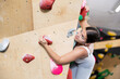 Young female alpinist practicing indoor a rock-climbing on a artificial boulder without the safety belts