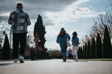 Wall Mural - A group of friends bounding down a path lined with neat trees under a bright sky, engaging in lively and joyful interaction.