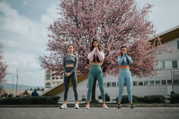 Wall Mural - Active young women in sportswear standing confidently outdoors with blooming cherry blossoms in the background.