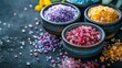 Various types of colorful bath salts in ceramic bowls scattered on a dark surface, highlighting the beauty and variety of spa essentials, concept of relaxation and body care.