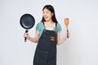 Young woman wearing kitchen apron cooking and holding pan and spatula isolated on white background.