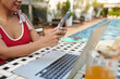 © DragonImages - Cropped image of woman in swimsuit answering text messages and emails when working by pool
