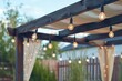 Textile awning and wooden frame gazebo with retro edison light bulbs glowing on sunny summer day in backyard