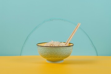 Wall Mural - Korean ramen and chopsticks in a bowl on yellow and blue background from the front