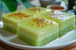 Slices of Puding Lumut or Pandan Cheese Pudding covered with vla milk served on a white ceramic plate in close up