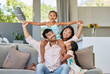 © peopleimages.com - Portrait, parents and kids on sofa with airplane game, bonding and relax together in living room on weekend. Mom, dad and girl children on couch with fun, support and playing in home in Indonesia.