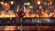 A glass of red wine is sitting on a wooden bar counter. The wine is almost empty, with only a small amount of liquid left in the glass. The bar is dimly lit, creating a cozy and intimate atmosphere