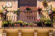Ein mit bunten Zierblumen geschmückter kleiner Balkon mit schmiedeeiserner Balustrade in mediterranem Stil bei Sonnenschein und geschlossener Balkontür