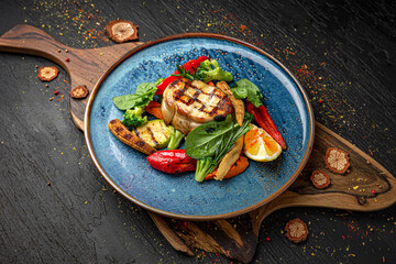 Wall Mural - Sturgeon steak with roasted vegetables. Menu for a pub on a dark background. Colorful juicy food photography.