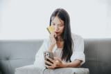 Fototapeta  - Asian woman with smartphone and credit card sitting on sofa Thinking about buying products online on the internet. online shopping concept Online payment via credit card Mobile Banking
