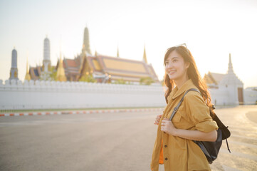 Wall Mural - Traveler asian woman in her 30s, backpack slung over her shoulder, explores the intricate details of Wat Pra Kaew with childlike wonder. Sunlight dances on the golden rooftops.