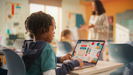 Wall Mural - Teacher Explaining a Math Lesson to a Classroom Full of Bright Diverse Children in Primary School. Little Black Boy Browsing a Presentation on a Laptop Computer