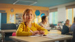 © Gorodenkoff - Portrait of a Cute Smiling Redhead Girl Sitting Behind a Desk in Class in Elementary School. Young Pupil is Looking at Camera, Smiling. Kids Educated in Modern Primary School