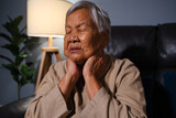 Fototapeta Lawenda - senior woman suffering from neck pain while sitting on sofa in living room at night