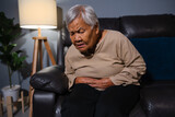 Fototapeta Lawenda - senior woman suffering from stomach ache  while sitting on sofa in the living room at night
