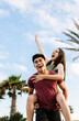 © Xavier Lorenzo - Vertical portrait of happy young multiracial couple having fun together on summer vacation. Joyful asian man piggybacking pretty woman outdoors. Love, happiness and friendship concept