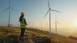 Engineer with wind turbines evaluates renewable energy at sunset