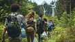 A group of students dressed in casual clothes lugging large bags and containers as they hike through a lush forest. In the background wind turbines can be seen spinning silently highlighting .