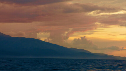 Wall Mural - Sunset over a tropical island. View of the silhouette of a tropical island and clouds colored by the rays of the setting sun.