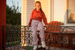 Smiling cheerful satisfied Caucasian little girl sitting on terrace at home wearing casual clothing looking at camera with delighted facial expression