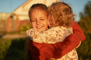 Cheerful joyful smiling siblings playing together outdoor hugging embracing each other elder sister closing eyes with pleasure kids playing on street near their house