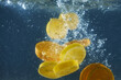 Tropical fruits oranges and lemons dropped into water with splashing isolated over dark blue background