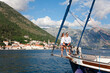 Happy couple traveling on yacht at sea. Travelers sailing, enjoying summer vacation. Tourists have adventure on sailboat. Gorgeous landscape with beautiful mountains, coast. Perast, Montenegro