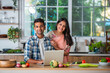 Happy Indian asian smart couple having fun in kitchen using laptop while cooking
