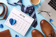 Flat lay composition for Father's Day featuring a calendar, tie, coffee cup, glasses, and shoes over a light blue backdrop