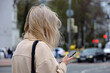 Girl with blond hair using smartphone on city street on blurred cars backgrounds