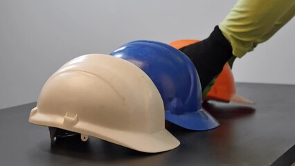 Wall Mural - Closeup of four hard hats in white, blue, orange and yellow color, placed on a wooden surface in a row being picked up one-by-one by construction workers