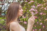 Fototapeta  - Brunette fashion model with long brown hair and natural makeup against floral background outdoor