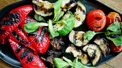 Wall Mural - A black plate of grilled peppers, cherry tomatoes, zucchini, eggplant and mushrooms