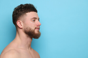 Poster - Handsome man with moisturizing cream on his face against light blue background, space for text