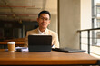 Portrait of Asian businessman in eyeglasses sitting with digital tablet and looking at camera
