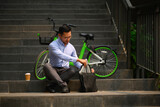 Fototapeta Nowy Jork - Shot of businessman with briefcase sitting on stairs in the city near his bicycle